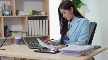 Bilgisayarı ve finansal belgeleri olan genç Asyalı kadın çalışanlar ofis masasında gülümsüyor ve grafikleri gösteren bilgisayarlarla çalışıyor. başlangıç iş fikri