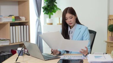 Bilgisayarı ve finansal belgeleri olan genç Asyalı kadın çalışanlar ofis masasında gülümsüyor ve grafikleri gösteren bilgisayarlarla çalışıyor. başlangıç iş fikri