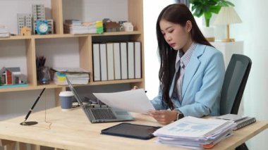 Bilgisayarı ve finansal belgeleri olan genç Asyalı kadın çalışanlar ofis masasında gülümsüyor ve grafikleri gösteren bilgisayarlarla çalışıyor. başlangıç iş fikri