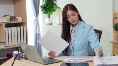 Bilgisayarı ve finansal belgeleri olan genç Asyalı kadın çalışanlar ofis masasında gülümsüyor ve grafikleri gösteren bilgisayarlarla çalışıyor. başlangıç iş fikri