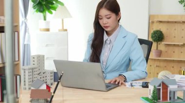 Bilgisayarı ve finansal belgeleri olan genç Asyalı kadın çalışanlar ofis masasında gülümsüyor ve grafikleri gösteren bilgisayarlarla çalışıyor. başlangıç iş fikri