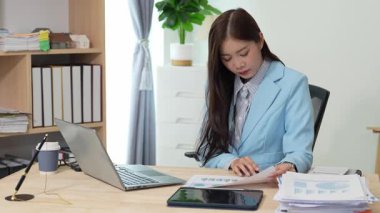 Bilgisayarı ve finansal belgeleri olan genç Asyalı kadın çalışanlar ofis masasında gülümsüyor ve grafikleri gösteren bilgisayarlarla çalışıyor. başlangıç iş fikri