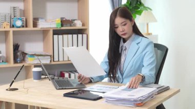 Bilgisayarı ve finansal belgeleri olan genç Asyalı kadın çalışanlar ofis masasında gülümsüyor ve grafikleri gösteren bilgisayarlarla çalışıyor. başlangıç iş fikri