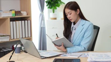 Bilgisayarı ve finansal belgeleri olan genç Asyalı kadın çalışanlar ofis masasında gülümsüyor ve grafikleri gösteren bilgisayarlarla çalışıyor. başlangıç iş fikri