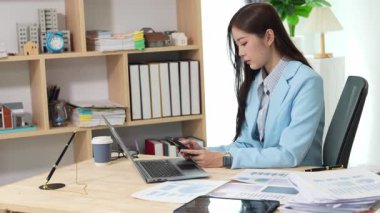 Bilgisayarı ve finansal belgeleri olan genç Asyalı kadın çalışanlar ofis masasında gülümsüyor ve grafikleri gösteren bilgisayarlarla çalışıyor. başlangıç iş fikri