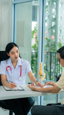 Doktor, yaşlı bir Asyalı erkek hastaya diz ağrısı için danışmanlık ve tedavi sağlıyor. Klinikteki diz ağrısını dindirmek ve sağlığınıza dikkat etmek için önerilen yöntemlerle birlikte..