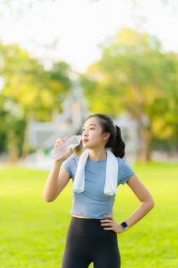 Genç Asyalı kadın dışarıda egzersiz yaptıktan sonra şişeden su içiyor. Parkta biraz dinleniyor..