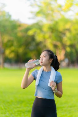 Genç Asyalı kadın dışarıda egzersiz yaptıktan sonra şişeden su içiyor. Parkta biraz dinleniyor..