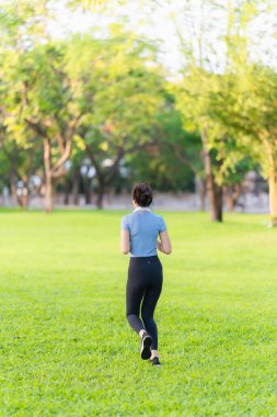 Asyalı kadın şehir parkında koştuktan sonra vücudunu ve boynunu uzatıyor, açık hava sporlarının tadını çıkarıyor..