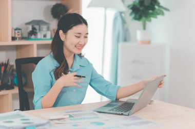 Genç Asyalı muhasebeci masada oturmuş belgeleri analiz ediyor. Şirket projeleri üzerinde çalışan grafikleri analiz ediyor..