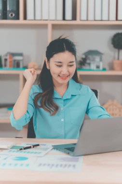 Genç Asyalı kadın muhasebeci iyi satışlar için heyecanlı ve masanızdaki satış performansınızdan memnun olduğunuzu ifade edin..