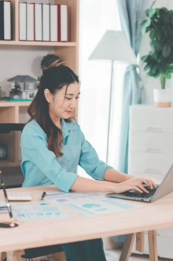 Genç Asyalı muhasebeci masada oturmuş belgeleri analiz ediyor. Şirket projeleri üzerinde çalışan grafikleri analiz ediyor..