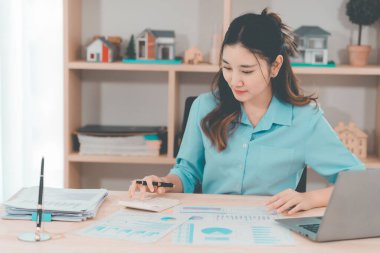 Genç Asyalı muhasebeci masada oturmuş belgeleri analiz ediyor. Şirket projeleri üzerinde çalışan grafikleri analiz ediyor..