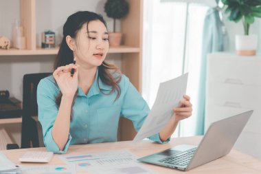 Genç Asyalı muhasebeci masada oturmuş belgeleri analiz ediyor. Şirket projeleri üzerinde çalışan grafikleri analiz ediyor..