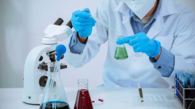 Medical researcher, chemist, examines samples under a microscope, pharmaceutical focus in lab coat, analyzes test tubes in work area.