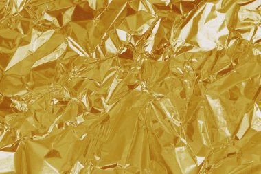 Altın folyo yaprağının parlak dokusu, arkaplan ve tasarım çalışmaları için soyut sarı ambalaj kağıdı.