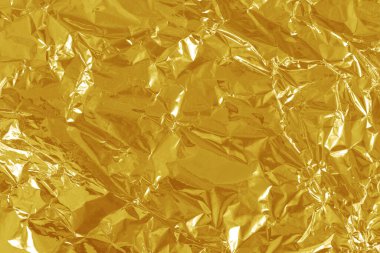 Altın folyo yaprağının parlak dokusu, arkaplan ve tasarım çalışmaları için soyut sarı ambalaj kağıdı.
