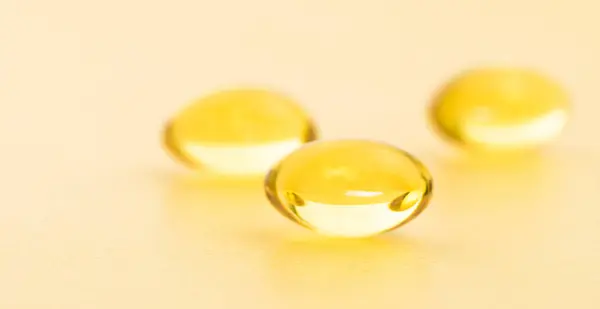 Fish oil supplement capsules on gold background. Cosmetics, omega 3 golden bubble. Gold oil capsules. Vitamin round pill set.