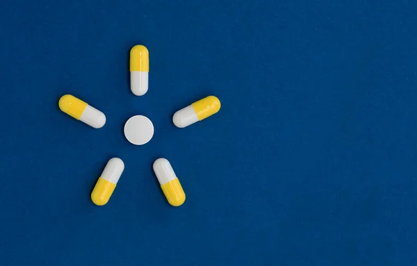 Summer yellow sun from pills tablets on blue surface with copy space. Minimalistic medicine concept.