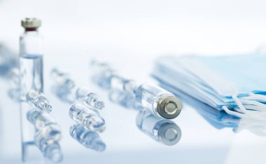 İğne için tıbbi ampuller ve tek kullanımlık maskeler. Masada ilaç bulunan dağınık cam ampuller..