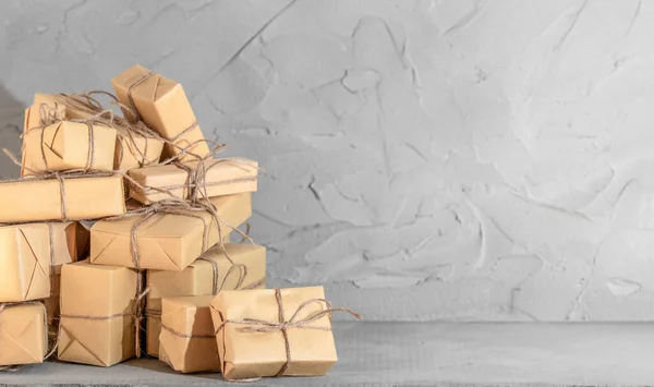 Many gift boxes in brown wrapping paper on the background of a concrete wall. Present box package with congratulation. Copy space.