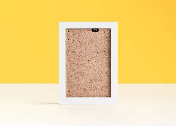 White blank photo frame on white table in front of yellow background with copy space