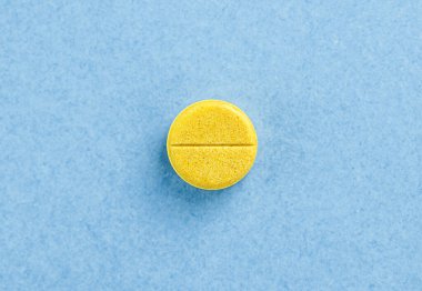 Tek sarı hap tableti. Mavi arkaplanda fotokopi alanı olan tablet. Sağlık kavramı