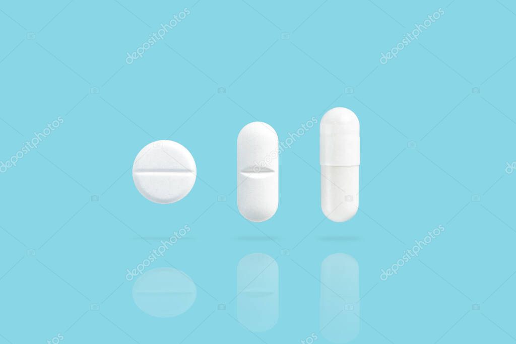 Various white medicine pills levitate over a blue background. Shadow and reflection from drugs.
