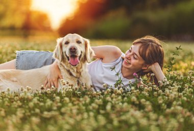 A Portrait of teenage girl petting golden retriever outside in sunset clipart