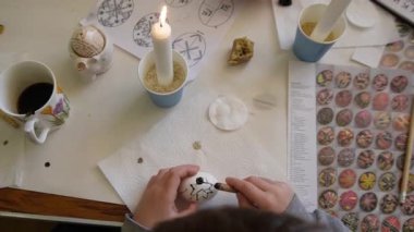 Paskalya yumurtasını balmumu ve boya metoduyla öldüren bir çocuk, balmumuna direnç tekniğini kullanarak yumurtayı dekore etme süreci, karmaşık desenler çizmek için geleneksel bir araç..