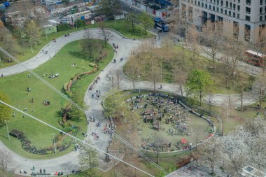 Aşağıdaki halka açık bir parkın canlı atmosferi, dolambaçlı yollar ve bir çocuk oyun alanı yayılan yeşil çimenler ve ağaçlar arasında hareketlenmeye başlıyor.