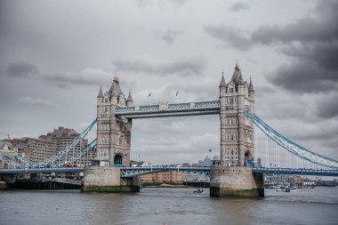 Kasvetli bulutlu gökyüzünün altındaki Londons Tower Köprüsü 'nün dramatik manzarası Viktorya dönemi Gotik mimarisini ve aşağıdaki işlek Thames Nehri' ni gözler önüne seriyor.