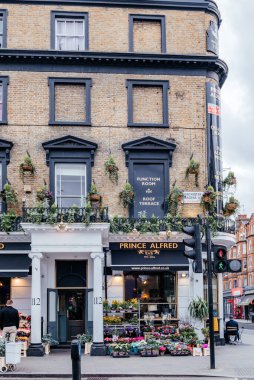 Londra 'nın hareketli bir sokağının cazibesine sahip tarihi Prens Alfred meyhanesi, sarkık bitkilerle süslenmiş ve renkli bir çiçek pazarıyla çevrili.