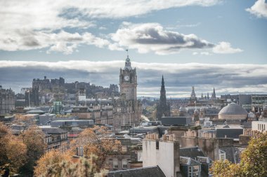 Edinburgh 'un panoramik manzarası parçalı bulutlu bir gökyüzü altında tarihi binalar ve simgeler sergiliyor.