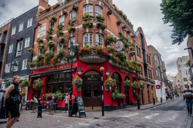 Londra 'daki hareketli bir sokak sahnesinde tarihi Crown and Anchor barı çiçek desenli cepheleriyle ve yaya geçitleriyle