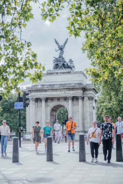 Güneşli bir günde Londra 'da Wellington Kemeri yakınlarında yürüyen 14 Temmuz 2024 Turistler, tarihi manzaranın ve çevreleyen yeşilliğin tadını çıkarıyorlar.