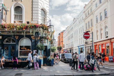 24 Temmuz 2024 Londra 'daki hareketli bir sokak sahnesinde canlı çiçeklerle süslenmiş tarihi bir bar ve canlı atmosferin tadını çıkaran insanlar.