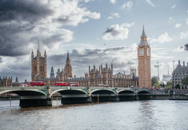 Big Ben ve Londra 'daki parlamento binalarının manzarası. Bulutlu bir gökyüzünün altında Westminster Köprüsü' nden geçen kırmızı çift katlı otobüsler.