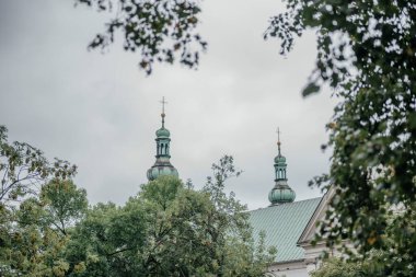 Krakow, Polonya 'daki yeşil kubbeli kilise kuleleri bulutlu bir günde kısmen yemyeşil ağaçlar tarafından gizlenmiş mimari ve doğa ile harmanlanmış.
