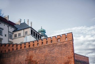 Krakow 'daki tarihi Wawel Şatosu' nda kırmızı tuğla tahkimatları, taş cepheleri ve bulutlu mavi gökyüzünün altındaki yeşil kuleye ev sahipliği yapıyor.