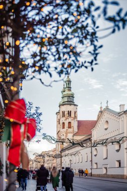 Krakow Eski Kasabası 'nda Noel süslemeleri, ışıkları ve arka planda tarihi bir kilise olan şenlikli bir cadde.