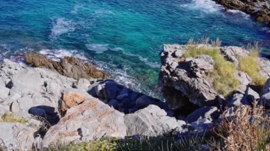 Dalgalardan yansıyan canlı turkuaz su ve güneş ışığıyla kayalık bir sahil manzarası rahatlama ve seyahat temaları için mükemmel.