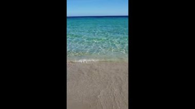 Turkuaz Akdeniz dalgalarının kumlu bir kıyıya vuruşunu gösteren dikey bir video, rahatlama ve meditasyon için mükemmel.