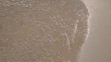 Yumuşak okyanus dalgalarının rahatlatıcı görüntüsü güneşli kumlu kıyılarda köpük desenleri yaratıyor, rahatlama ve kıyı temaları için mükemmel.