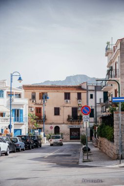 Sicilya, Palermo 'da sakin bir cadde. Geleneksel Akdeniz binaları, park edilmiş arabalar ve güneşli bir gökyüzünün altındaki uzak dağ manzarası.