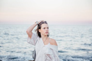 Günbatımında okyanus kenarında düşünceli poz veren genç bir kadın, yumuşak dalgalar ve arka planda pastel bir gökyüzü, Mondello, Sicilya yakınlarında.