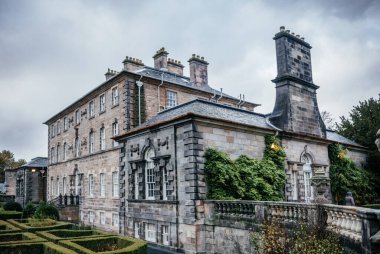 Pollock Evi, İskoçya 'da tarihi bir taş köşk, sarmaşık kaplı duvarlar, klasik mimari, ve bulutlu gökyüzünün altında güzel manikürlü bir bahçe.