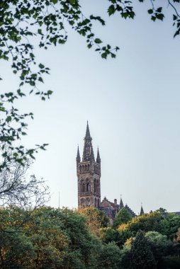 Açık bir yaz gününde yeşil ağaçlar tarafından çerçevelenmiş, eğitim, tarih ve mimariyi sembolize eden Glasgow Üniversitesi tarzı bir kule.