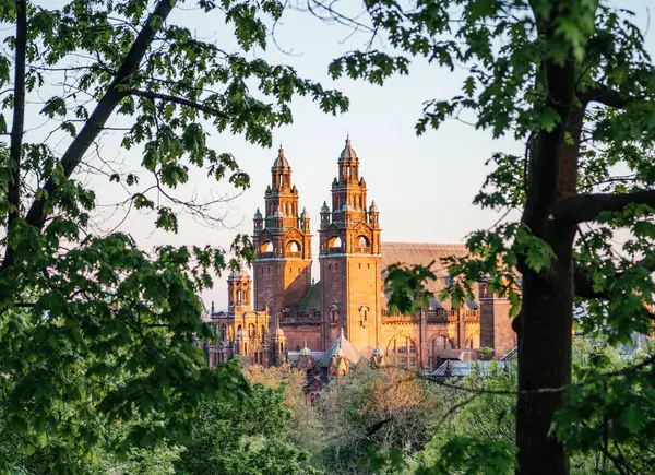 Glasgow 'daki Kelvingrove Sanat Galerisi ve Müzesi günbatımında ağaç dallarının arasından görülerek, tarihi mimarisi ve doğal çevresini ön plana çıkarıyor.