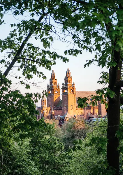 Glasgow 'daki Kelvingrove Sanat Galerisi ve Müzesi günbatımında ağaç dallarının arasından görülerek, tarihi mimarisi ve doğal çevresini ön plana çıkarıyor.